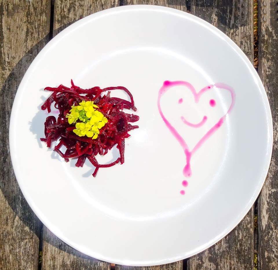 Hand-shredded fermented beetroot on a white plate with a heart drawn in beet juice
